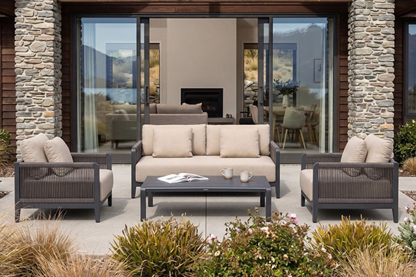 Dark aluminium outdoor lounge set with rope-weave armchairs and sofa on a stone patio, ideal for cooler South Island climates