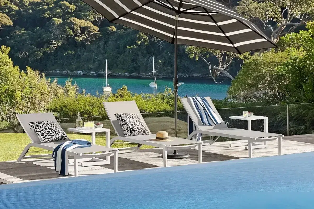 White aluminium sun loungers with umbrella beside a pool on a coastal NZ property