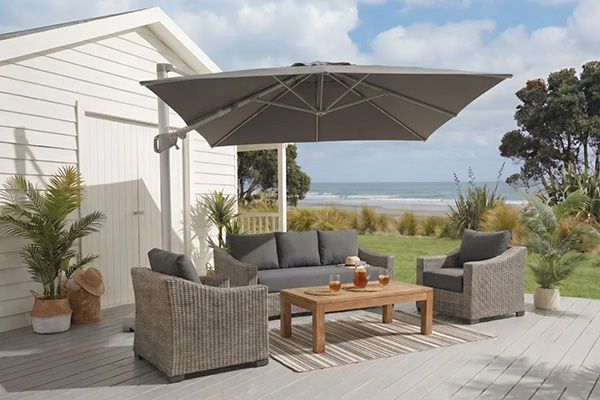 Wicker outdoor lounge set with cantilever umbrella on a coastal NZ deck overlooking the beach